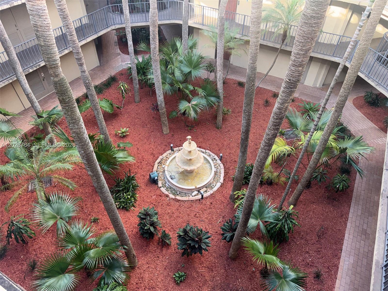 An elevated view of a courtyard featuring a central fountain, palm trees, and red mulch — 8625 NW 8th St # 402, Miami FL 33126, MIAMI, FL