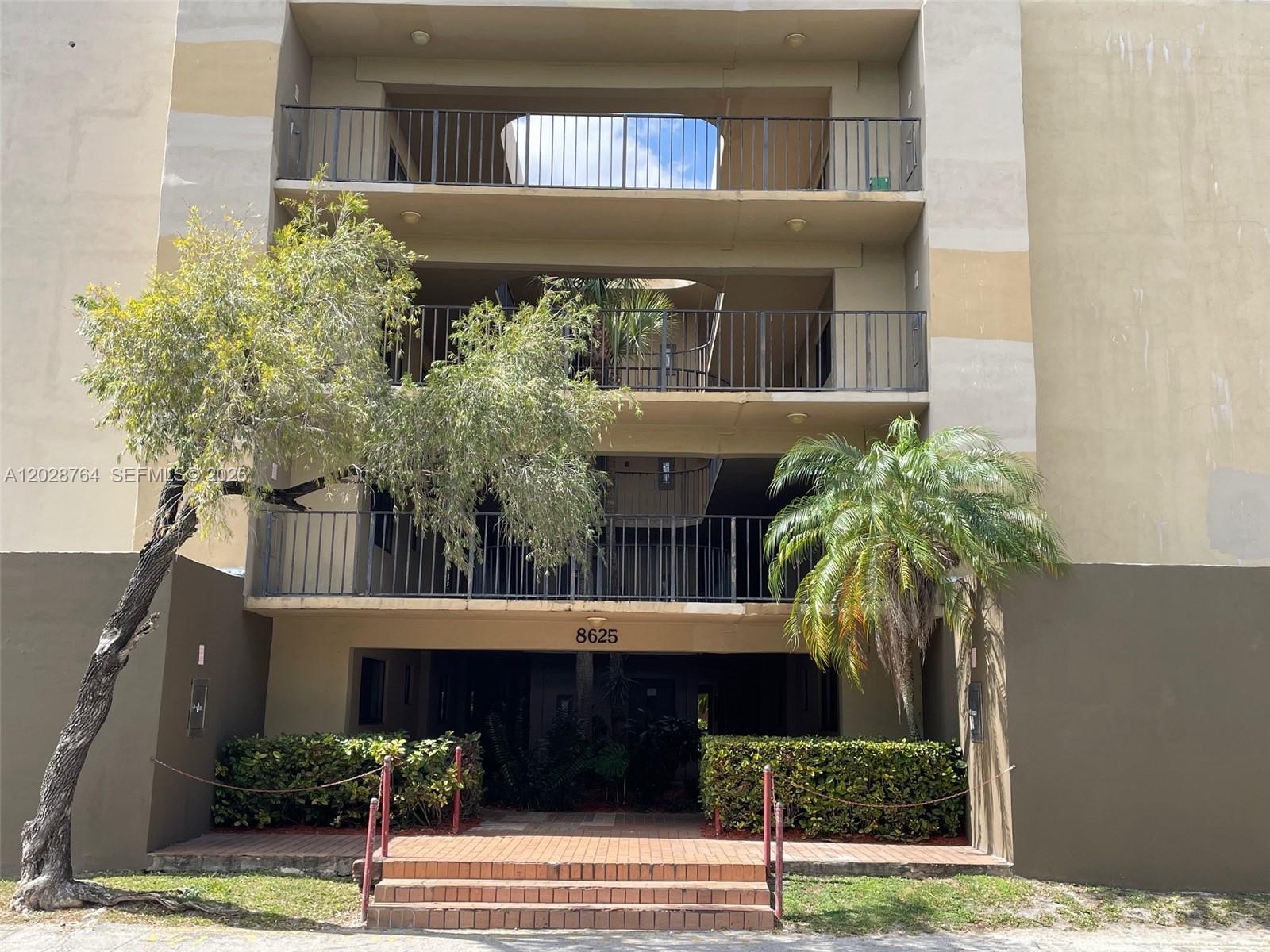 A three-story apartment building exterior features balconies, a central staircase, and a landscaped entrance — 8625 NW 8th St # 402, Miami FL 33126, MIAMI, FL