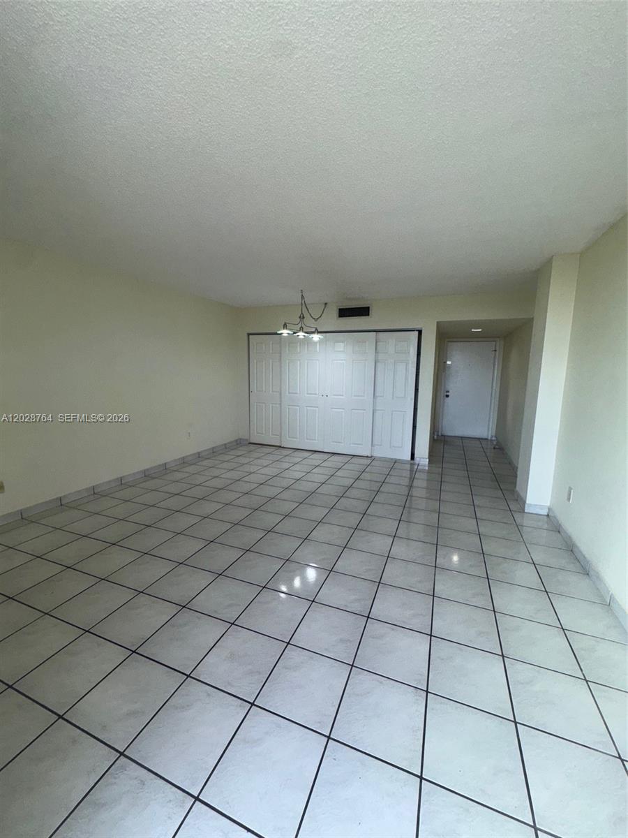 An empty room features white tiled floors, a popcorn ceiling, and a set of closet doors — 8625 NW 8th St # 402, Miami FL 33126, MIAMI, FL