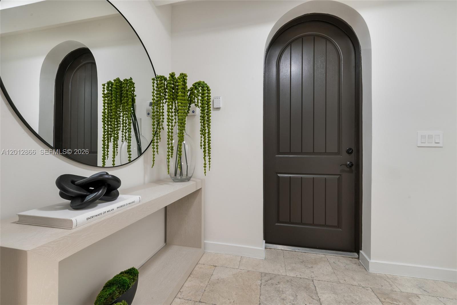 A modern entryway features a light wood console table, a round mirror, and an arched door — 345 Madeira Ave # 345, Coral Gables FL 33134, CORAL GABLES, FL