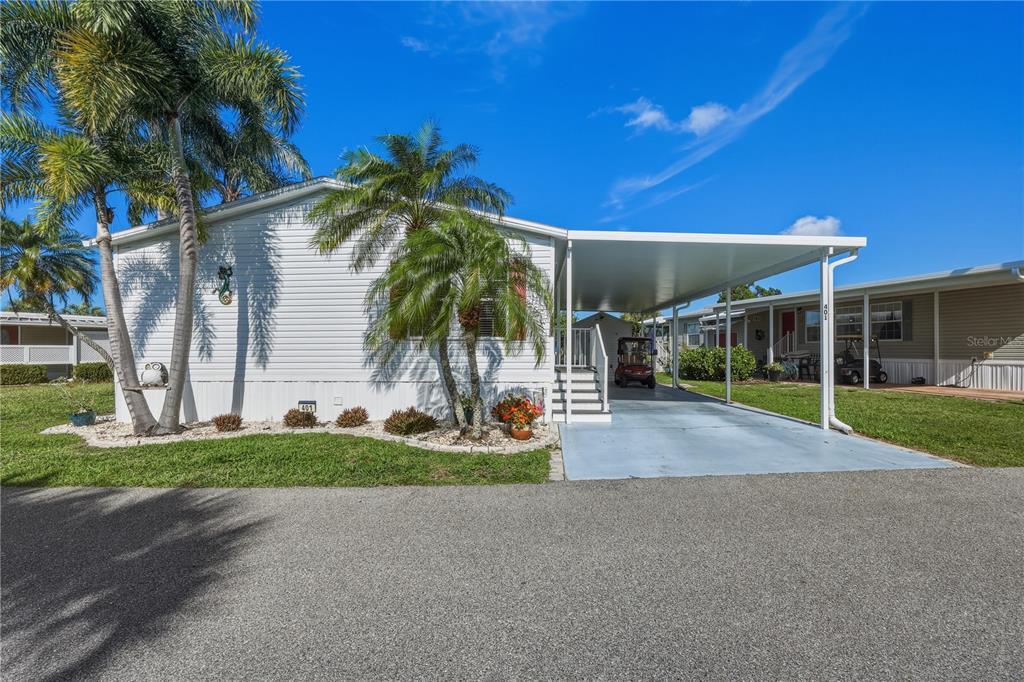 A white manufactured home with a carport, palm trees, and a paved driveway — 2100 KINGS HIGHWAY UNIT 401, PORT CHARLOTTE, FL