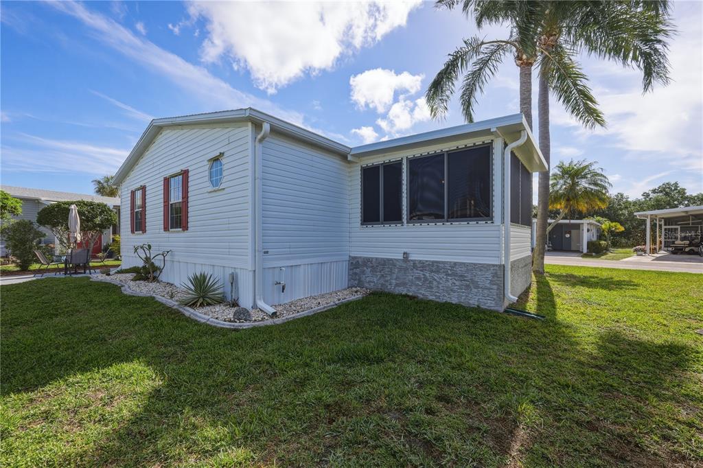 A white mobile home exterior features a screened-in porch, stone-textured skirting, and a palm tree — 2100 KINGS HIGHWAY UNIT 401, PORT CHARLOTTE, FL