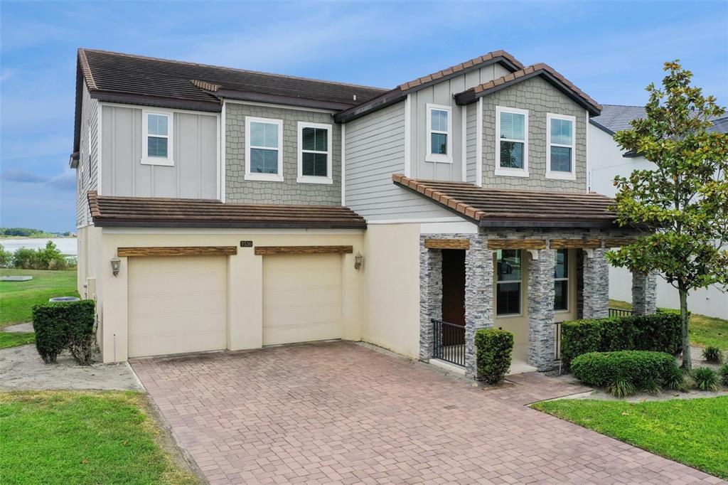A two-story house with a two-car garage, stone-accented entryway, and a brick paver driveway — 7530 ALPINE BUTTERFLY LANE, ORLANDO, FL