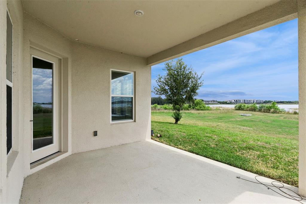 A covered concrete patio overlooks a grassy backyard with a view of a distant lake — 7530 ALPINE BUTTERFLY LANE, ORLANDO, FL