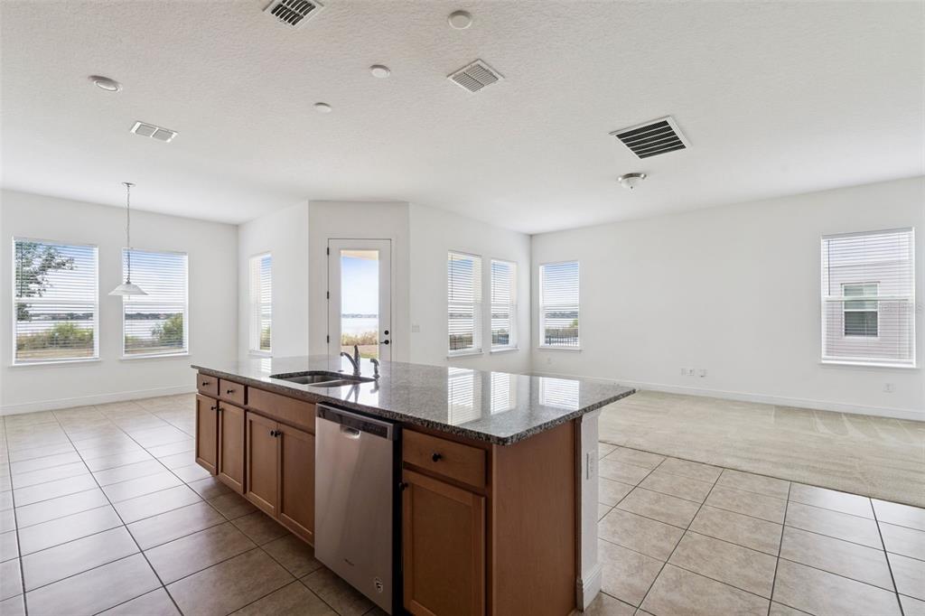 A kitchen island with granite countertops and stainless steel appliances overlooks a bright living area — 7530 ALPINE BUTTERFLY LANE, ORLANDO, FL