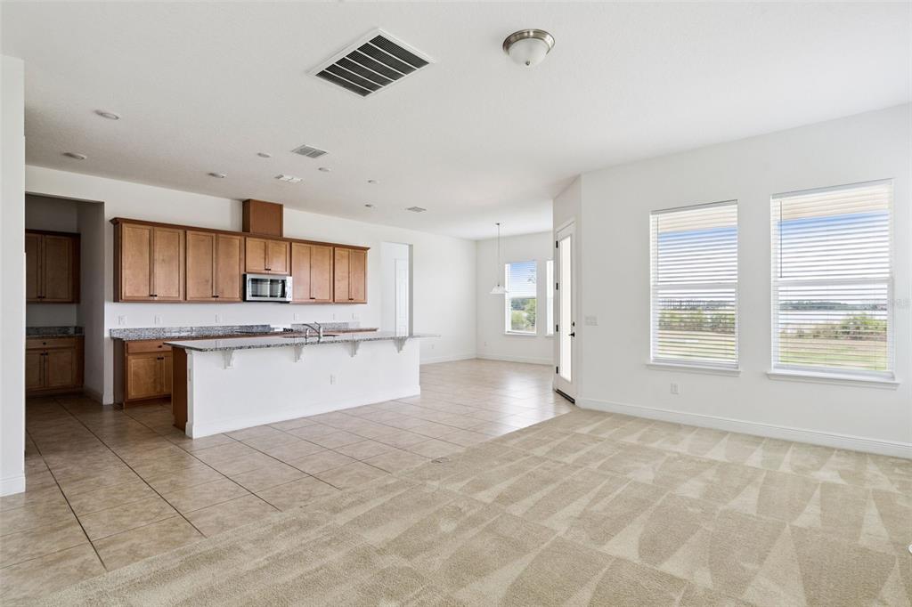 An open-concept kitchen and living area features wood cabinets, granite countertops, and tile flooring — 7530 ALPINE BUTTERFLY LANE, ORLANDO, FL