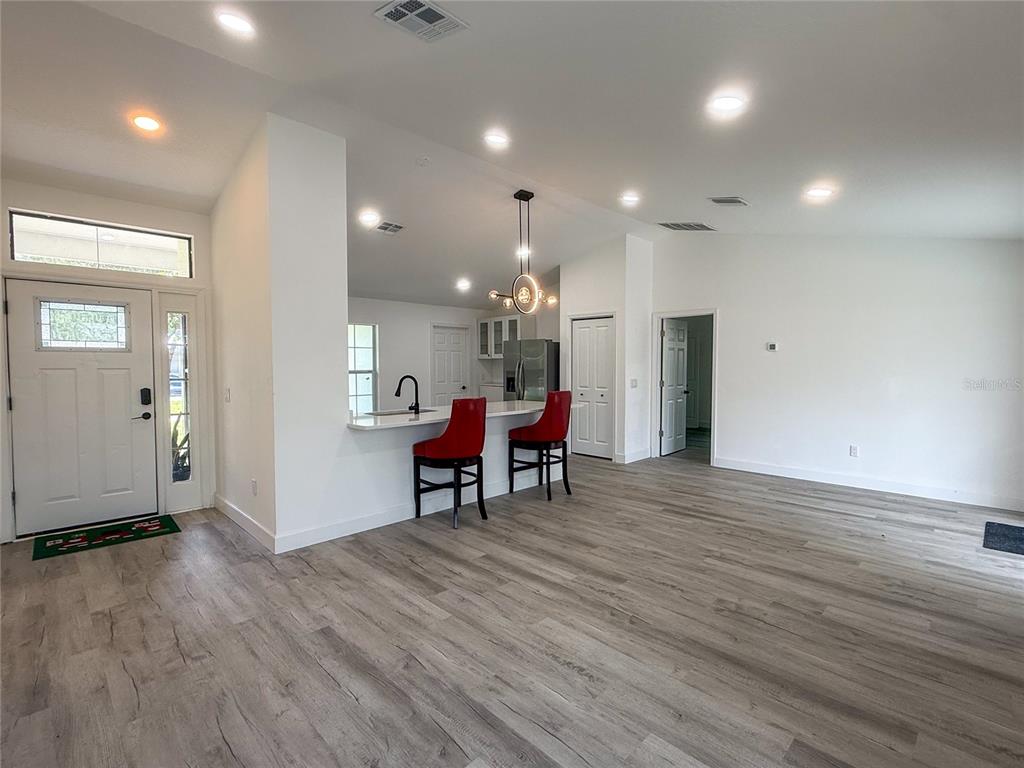 A bright open-concept living area features light wood-look flooring, a kitchen island with red stools, and a front entryway — 1367 HENSLEY DRIVE, DELAND, FL
