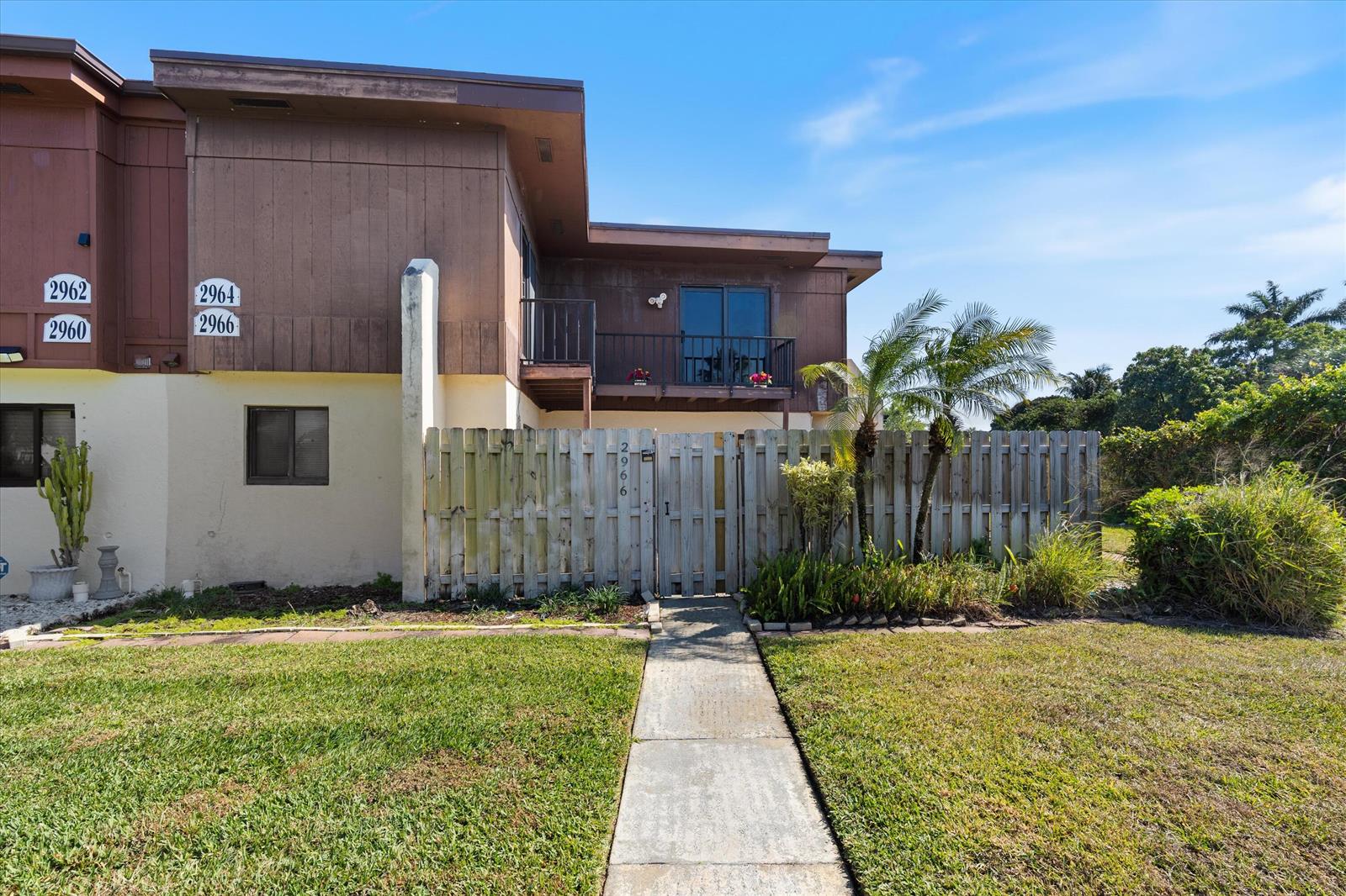 A two-story townhouse exterior features a wooden fence, a balcony, and a concrete walkway — 2966 Kirk Road, Lake Worth FL 33461, LAKE WORTH, FL