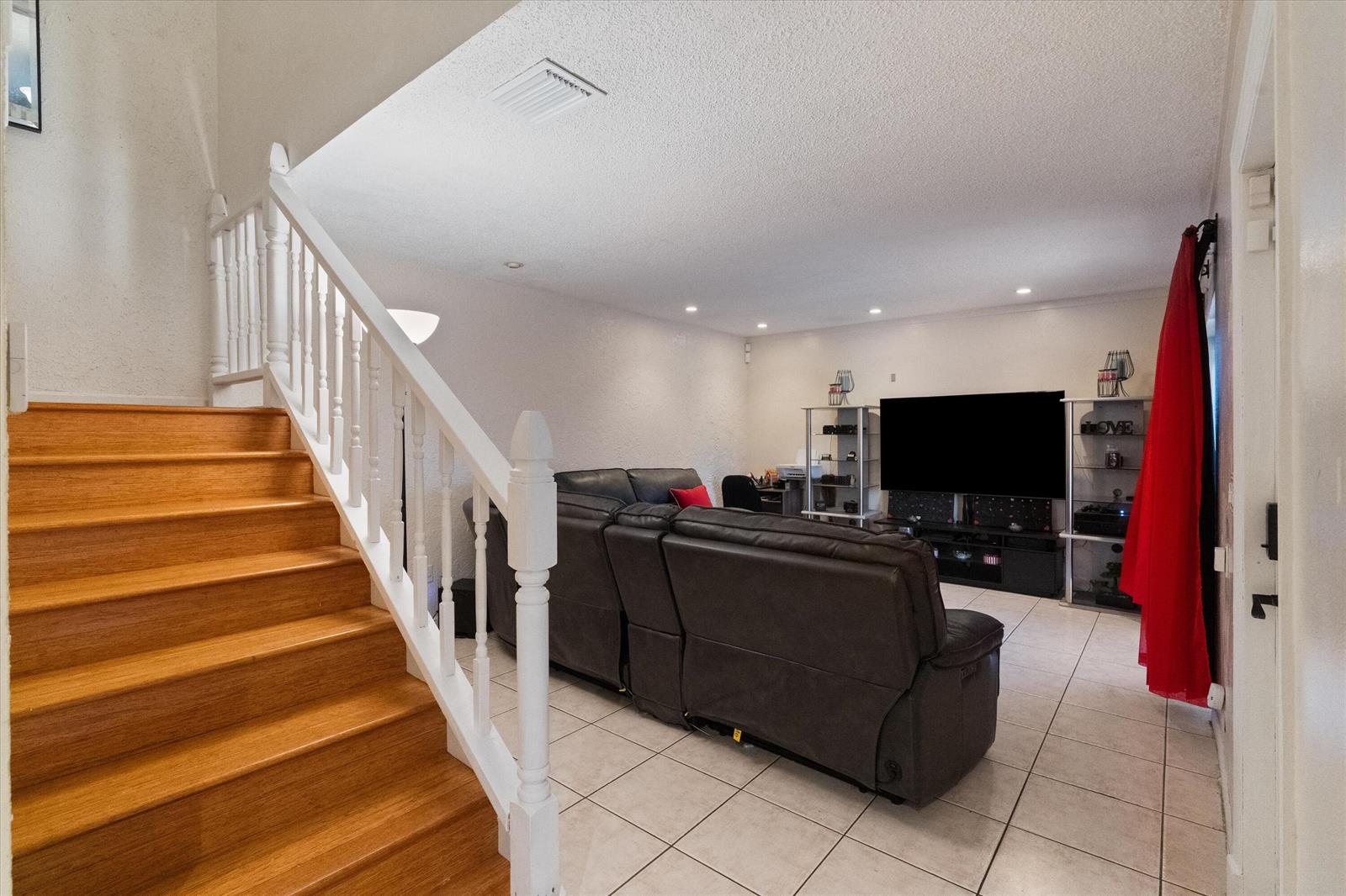 A living room features a wooden staircase, tile flooring, a dark leather sofa, and a television — 2966 Kirk Road, Lake Worth FL 33461, LAKE WORTH, FL
