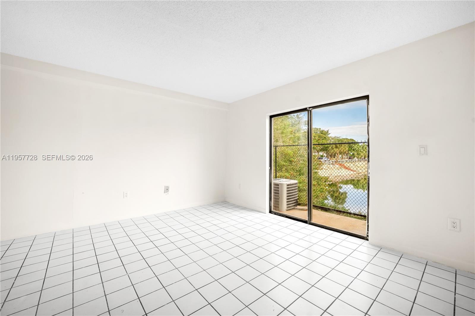 An empty room with white tile flooring and a sliding glass door overlooking a pond — 7805 SW 152nd Ave # 0, Miami FL 33193, MIAMI, FL