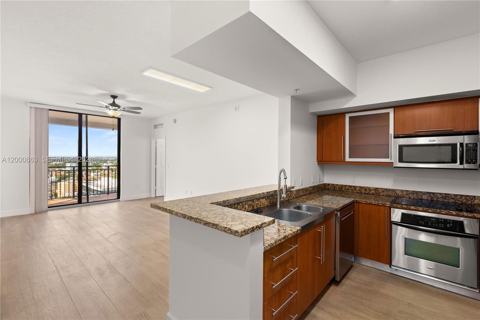 A kitchen with granite countertops and wood cabinets opens to a living area with balcony access — 888 S Douglas Rd, Coral Gables FL 33134, CORAL GABLES, FL