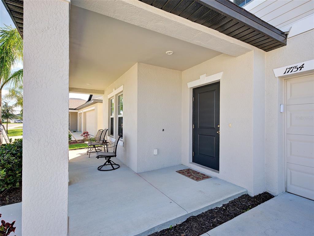 A covered concrete porch features a dark front door, two chairs, and a garage entrance — 17154 MONTE ISOLA WAY, NORTH FORT MYERS, FL