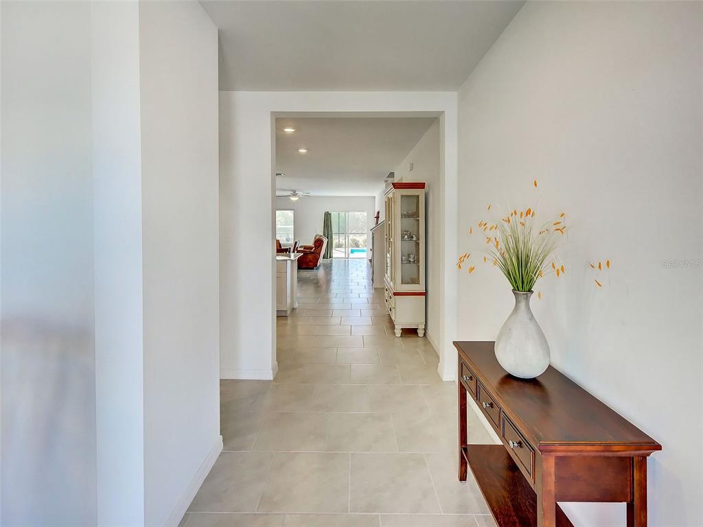 A hallway with light tile flooring leads toward a living area with a pool view — 17154 MONTE ISOLA WAY, NORTH FORT MYERS, FL