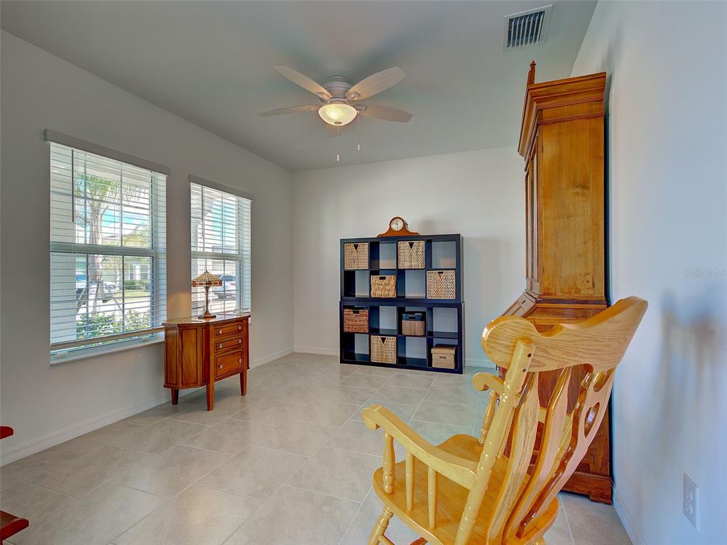 A room with tile flooring, a ceiling fan, windows, a bookshelf, and a wooden rocking chair — 17154 MONTE ISOLA WAY, NORTH FORT MYERS, FL