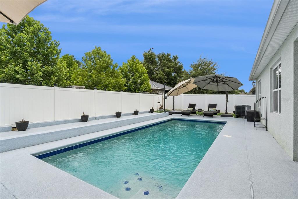 A backyard swimming pool with a concrete deck, tiered seating, and two patio umbrellas — 5946 CHURCHILL SQ WAY, GROVELAND, FL