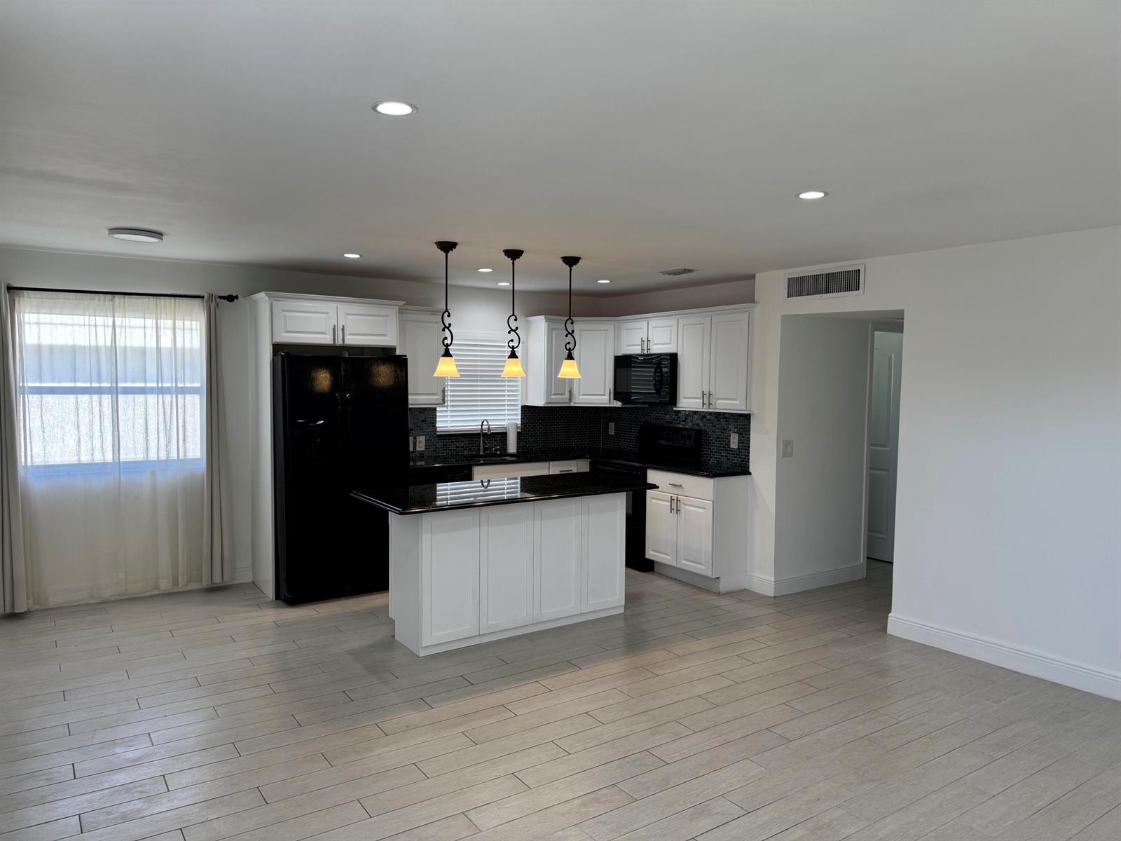 A kitchen features white cabinets, black countertops, a central island, and light wood-look flooring — 669 Monaco N, Delray Beach FL 33446, DELRAY BEACH, FL