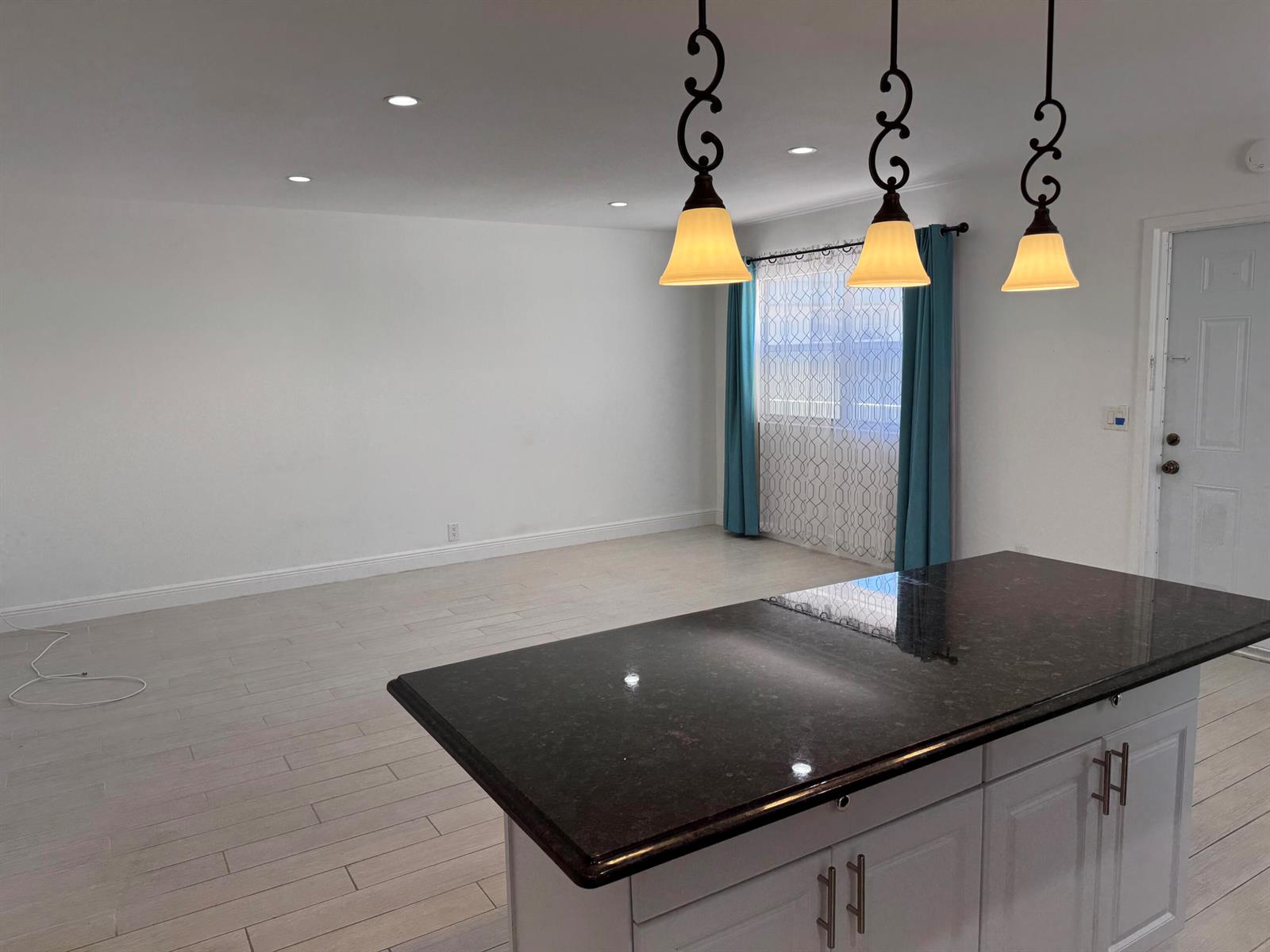 A kitchen island with a dark granite countertop sits before an open living area — 669 Monaco N, Delray Beach FL 33446, DELRAY BEACH, FL