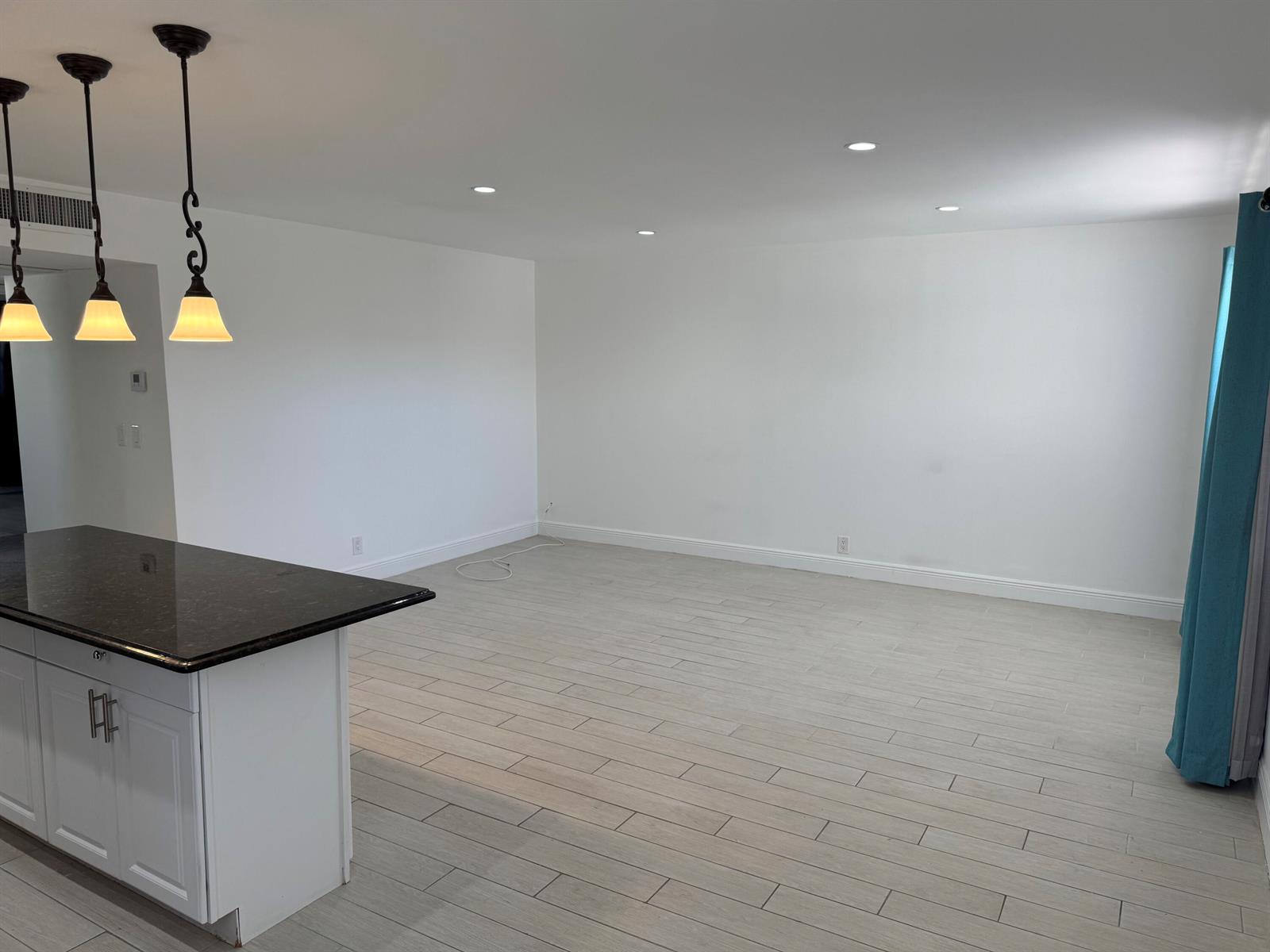 An open-concept living area features light wood-look tile flooring, white walls, and a kitchen island — 669 Monaco N, Delray Beach FL 33446, DELRAY BEACH, FL