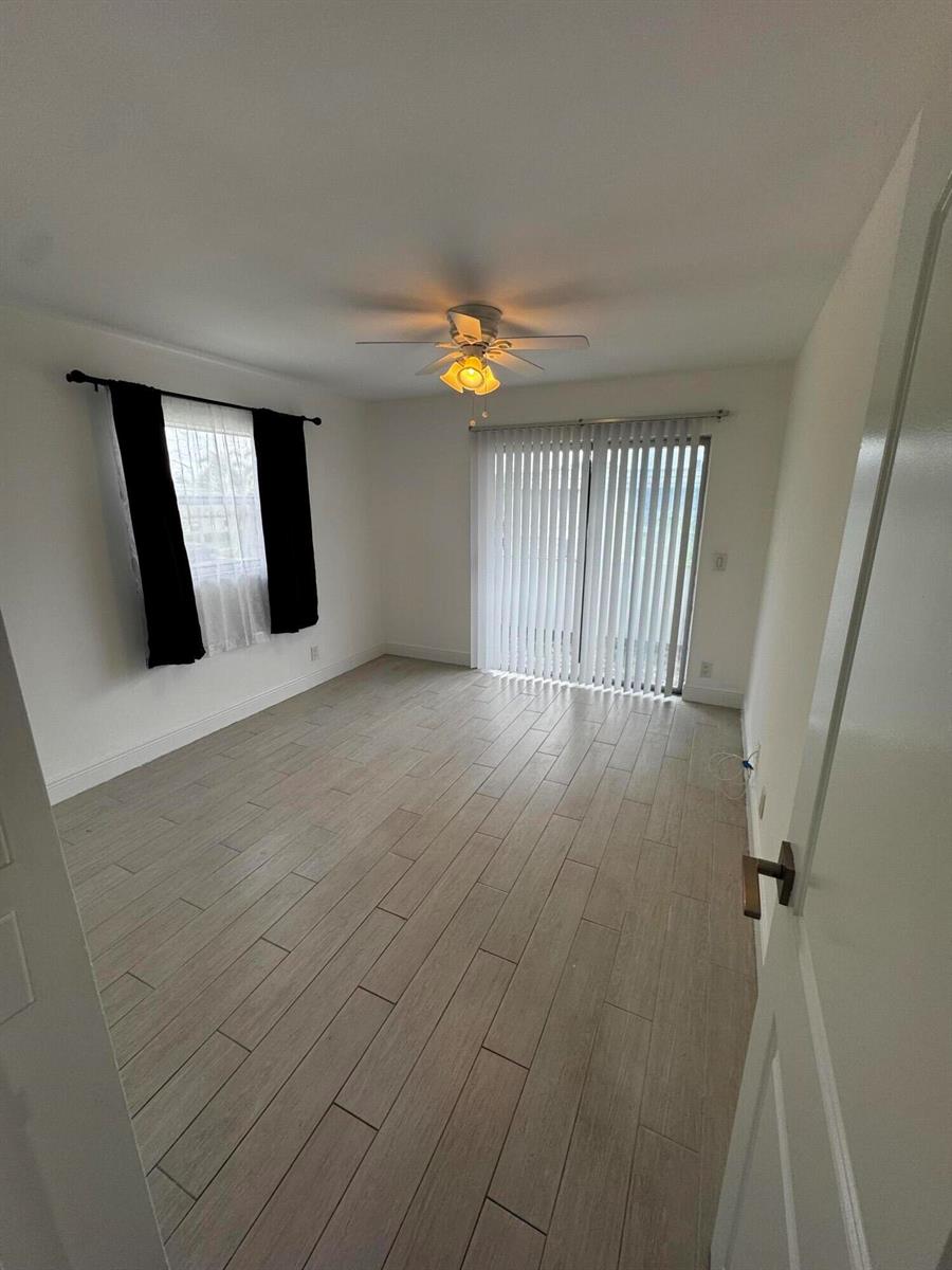 An empty room features light wood-look tile flooring, a ceiling fan, and vertical window blinds — 669 Monaco N, Delray Beach FL 33446, DELRAY BEACH, FL