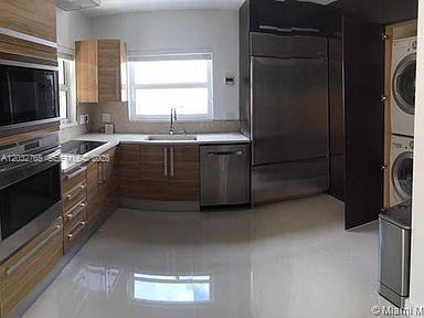 A modern kitchen features wood-grain cabinetry, stainless steel appliances, and a stacked washer and dryer — 3 Farrey Ln # 3, Miami Beach FL 33139, MIAMI BEACH, FL