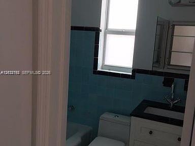 A bathroom features a white vanity with a black countertop, blue wall tiles, and a window — 3 Farrey Ln # 3, Miami Beach FL 33139, MIAMI BEACH, FL