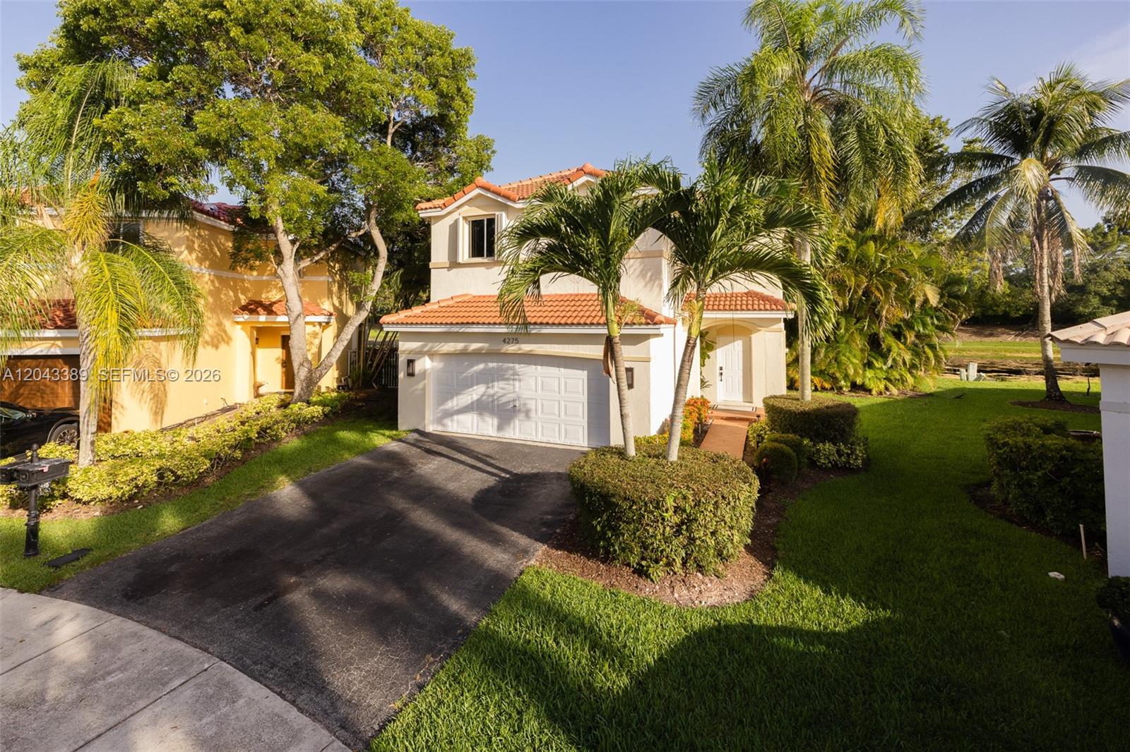 A two-story house with a tile roof, white garage door, and palm trees in front — 4275 Ironwood Ct, Weston FL 33331, WESTON, FL
