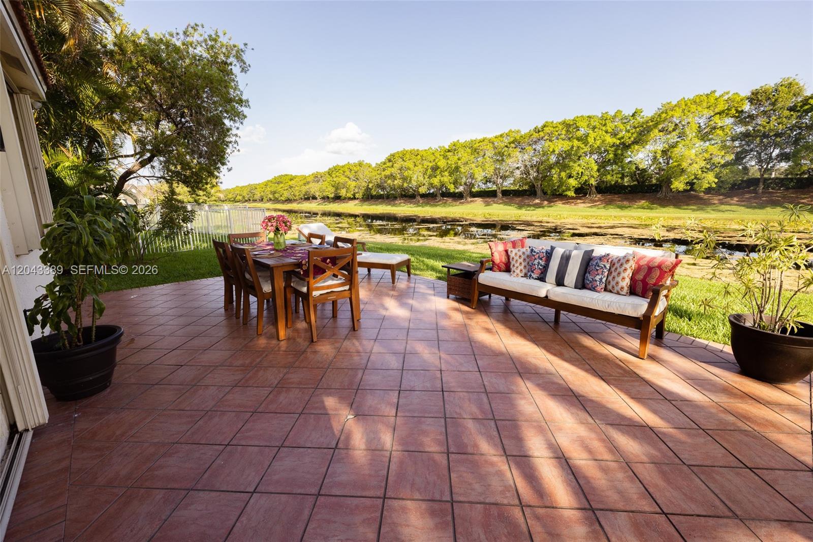 A tiled patio features outdoor dining furniture and a sofa overlooking a pond and trees — 4275 Ironwood Ct, Weston FL 33331, WESTON, FL