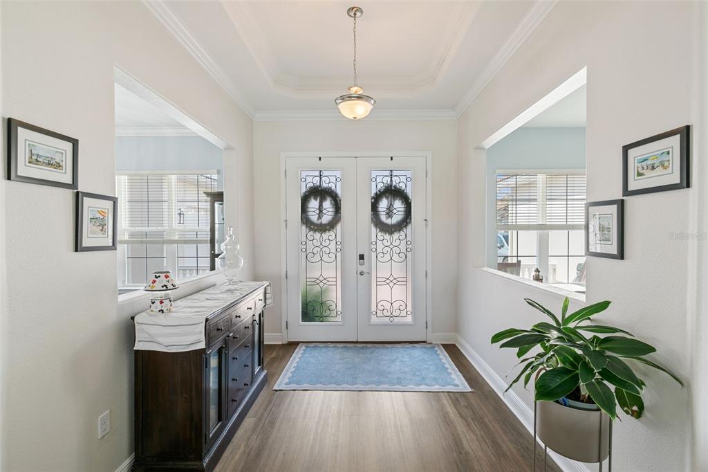 A bright foyer features double glass-paneled doors, wood-look flooring, a tray ceiling, and side cutouts — 3713 DOCKSIDE DR, KISSIMMEE, FL