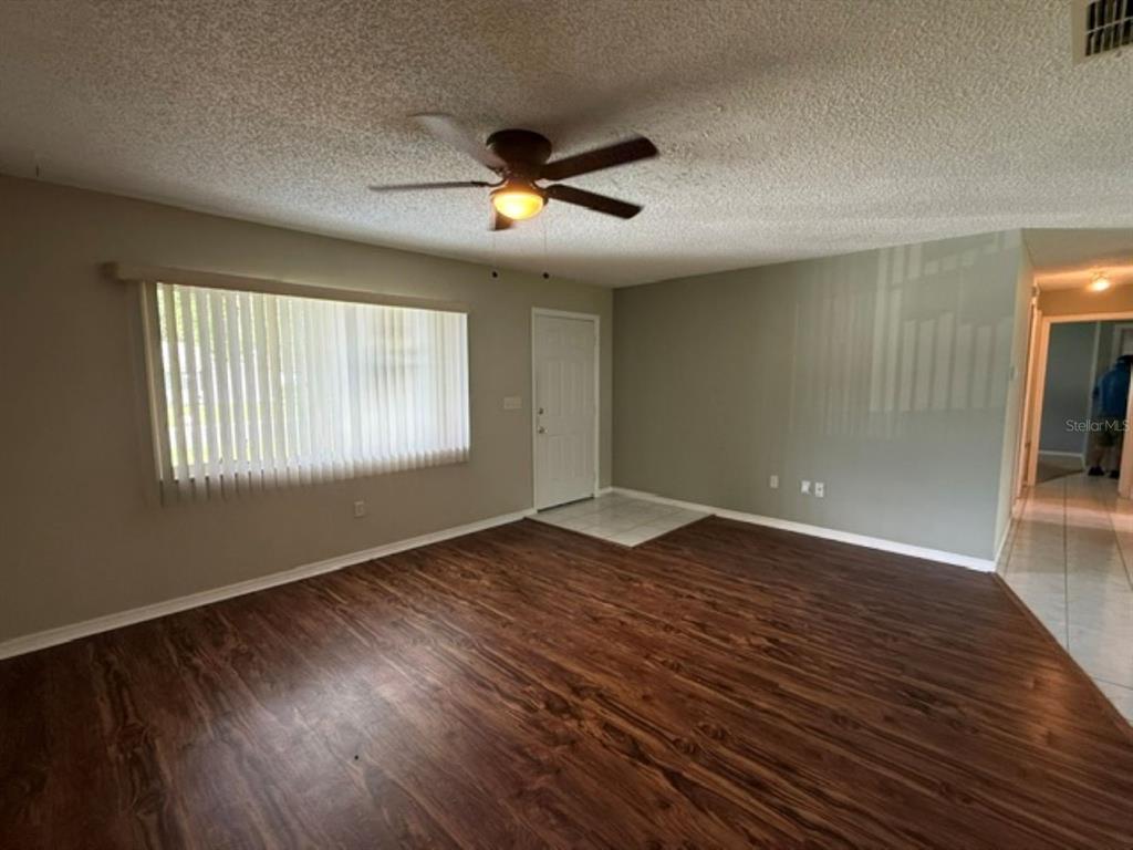 A living room features wood-look flooring, a ceiling fan, and a large window with blinds — 10235 SE 178TH PLACE, SUMMERFIELD, FL