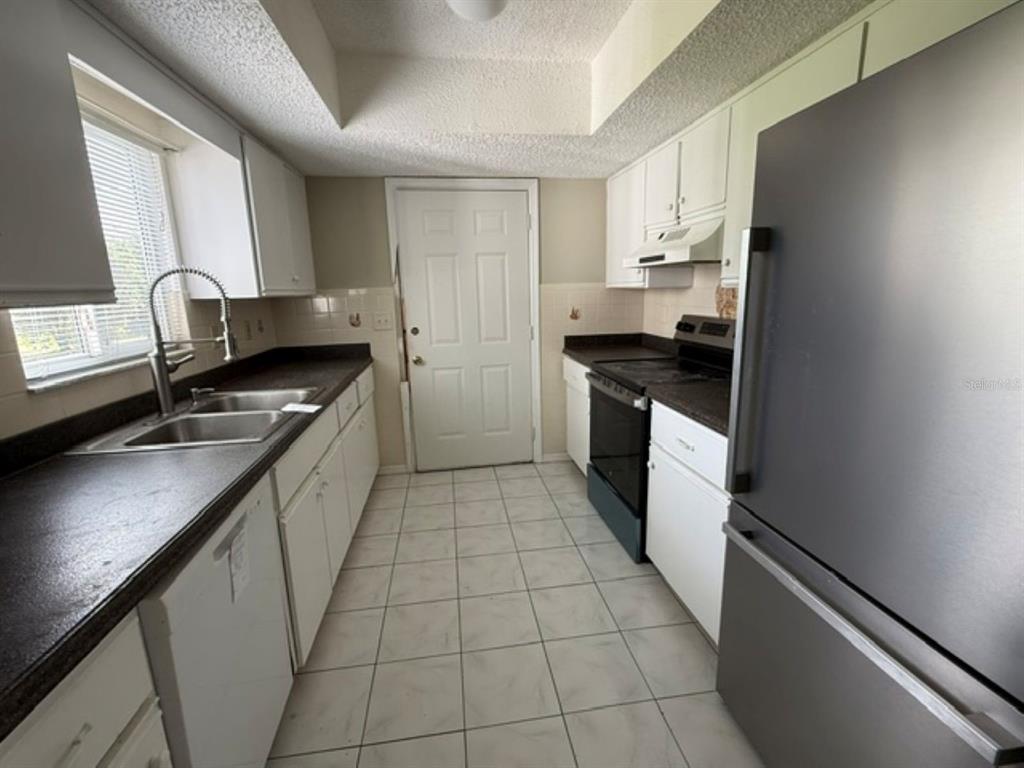 A galley kitchen features white cabinets, dark countertops, stainless steel appliances, and light tile flooring — 10235 SE 178TH PLACE, SUMMERFIELD, FL