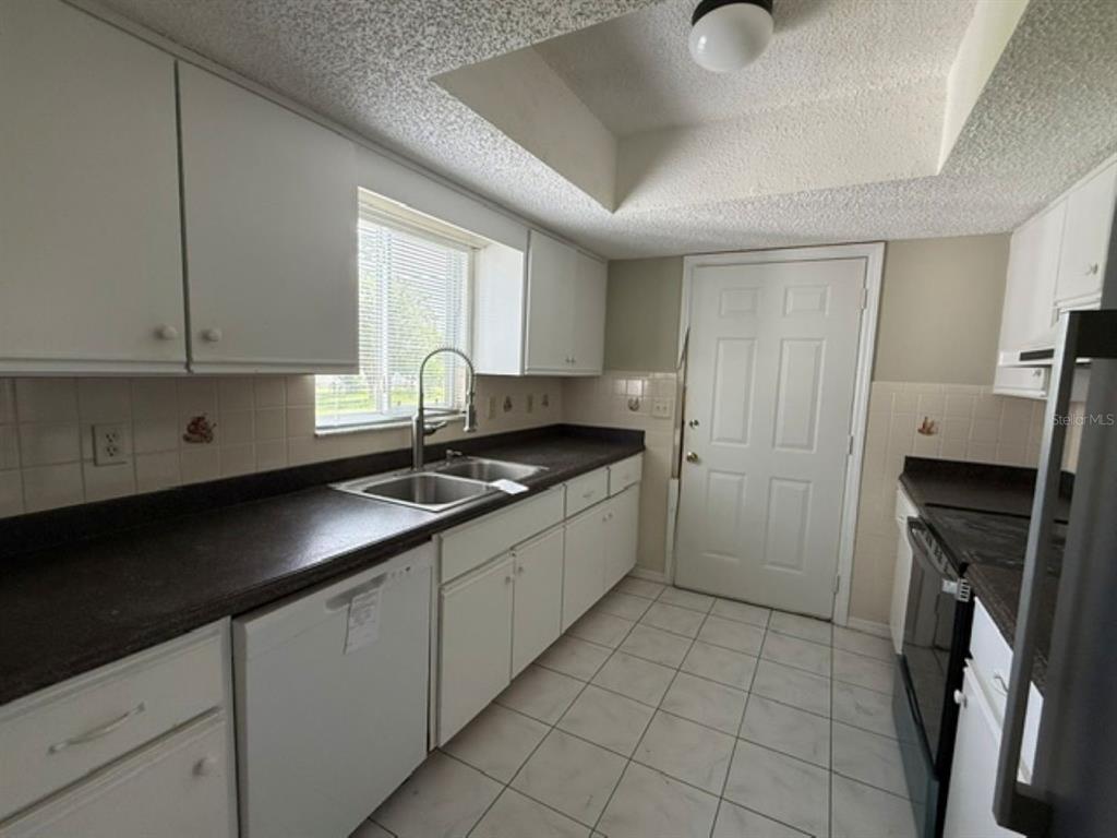 A kitchen with white cabinets, dark countertops, a double sink, and white tile flooring — 10235 SE 178TH PLACE, SUMMERFIELD, FL