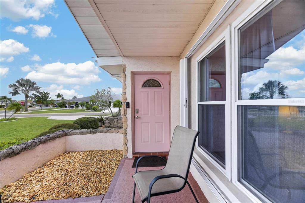 A pink front door and a patio chair sit on a covered porch with gravel — 907 BLUEWATER DRIVE, SUN CITY CENTER, FL