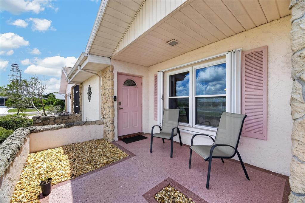 A front porch features two chairs, a pink door, and a small rock garden area — 907 BLUEWATER DRIVE, SUN CITY CENTER, FL