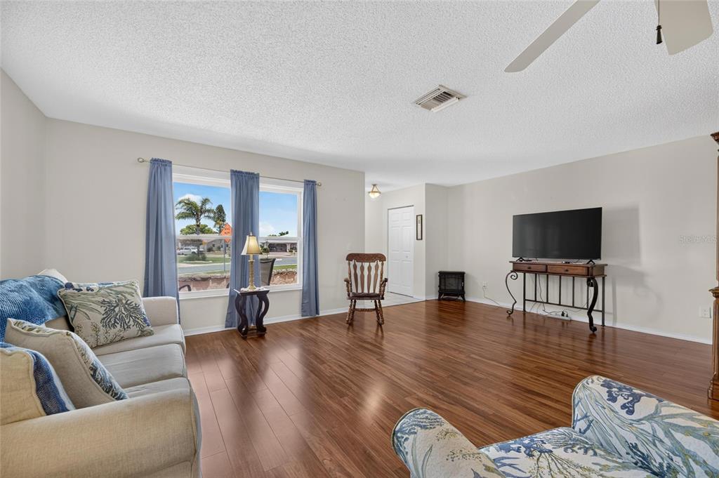 A living room with hardwood floors, a sofa, a television on a console, and windows — 907 BLUEWATER DRIVE, SUN CITY CENTER, FL