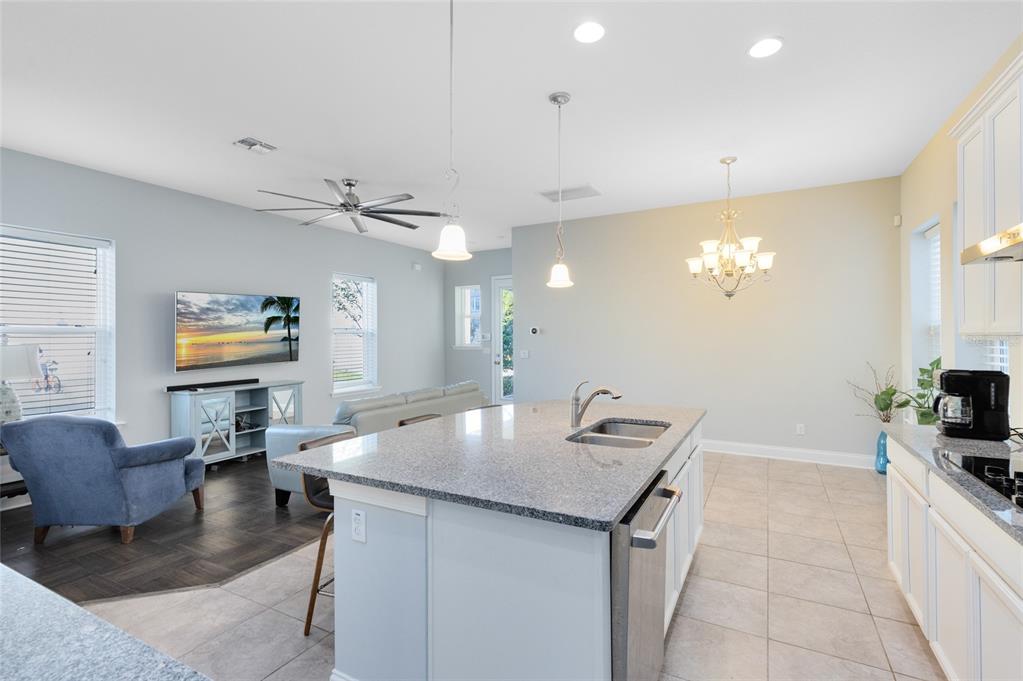 A bright kitchen features white cabinets, a granite island with stools, and tile flooring — 7749 LAUREATE BOULEVARD, ORLANDO, FL