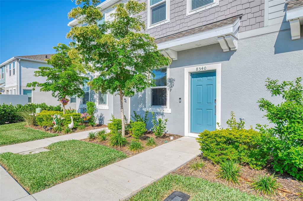 A light blue townhome exterior features a teal front door and a concrete walkway — 8540 DAYBREAK STREET, SARASOTA, FL