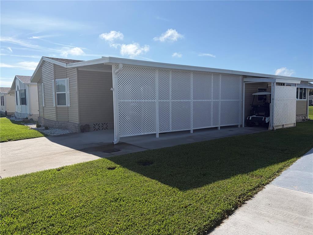 A mobile home exterior features a large carport enclosed by white lattice privacy screens — 57 STRAPHMORE DRIVE, HAINES CITY, FL