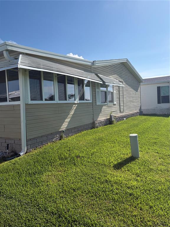 The exterior of a tan manufactured home features a screened-in porch and a grassy yard — 57 STRAPHMORE DRIVE, HAINES CITY, FL