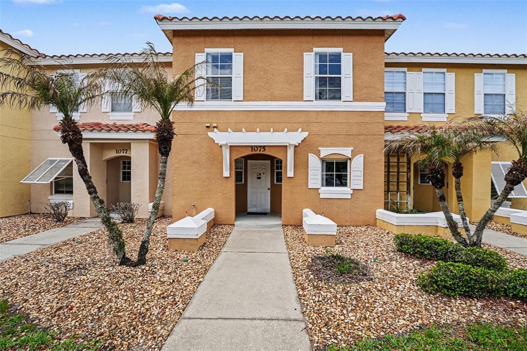 A two-story tan stucco townhouse with a central entrance and palm trees in the front — 1077 PARK RIDGE CIRCLE, KISSIMMEE, FL