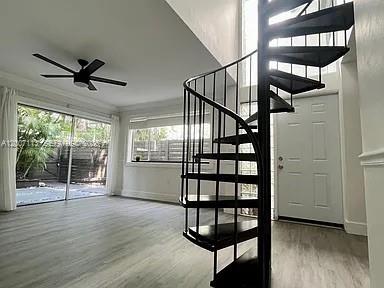A living room features light wood-look flooring, a ceiling fan, and a black spiral staircase — 3209 Bird Ave, Miami FL 33133, MIAMI, FL
