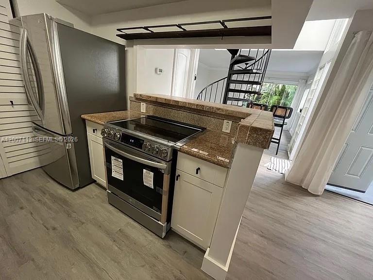 A kitchen features stainless steel appliances, granite countertops, and a spiral staircase in the background — 3209 Bird Ave, Miami FL 33133, MIAMI, FL