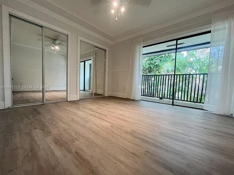 A bedroom with wood-look flooring, mirrored closet doors, and a sliding glass door to a balcony — 3209 Bird Ave, Miami FL 33133, MIAMI, FL