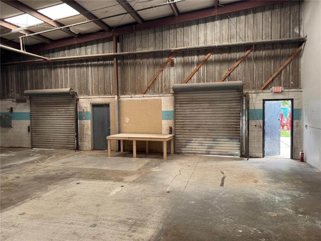 An industrial warehouse interior features concrete floors, two roll-up doors, and a wooden workbench — 2920 W AIRPORT BOULEVARD UNIT 130, SANFORD, FL