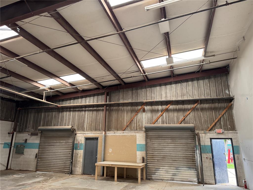 An industrial warehouse interior features two roll-up doors, a wooden workbench, and skylights — 2920 W AIRPORT BOULEVARD UNIT 130, SANFORD, FL