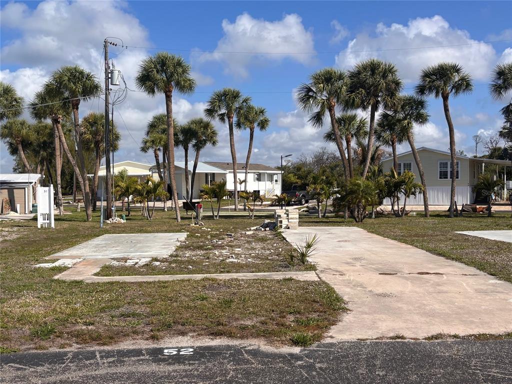 A vacant lot with a concrete pad and driveway sits among palm trees and houses — 7500 PARK POINTE DRIVE UNIT 52, ENGLEWOOD, FL