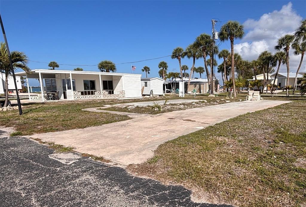 A concrete driveway leads to a white mobile home with a covered patio and palm trees — 7500 PARK POINTE DRIVE UNIT 52, ENGLEWOOD, FL