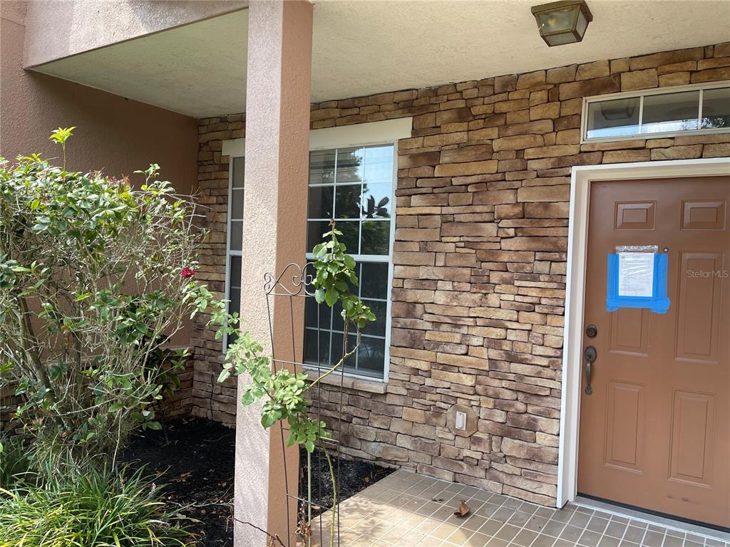 A brown front door with a notice sits beside a stone-veneer wall and window — 7617 BAY PORT ROAD UNIT 57, ORLANDO, FL