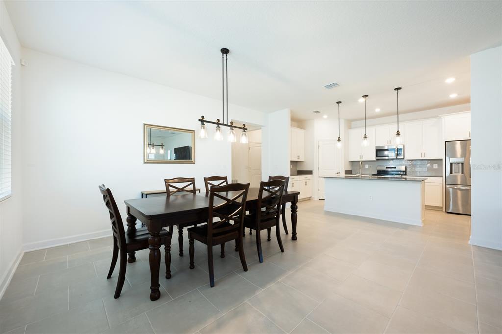 A dining area with a dark wood table and chairs adjacent to a modern kitchen — 1874 FLOURISH AVENUE, KISSIMMEE, FL