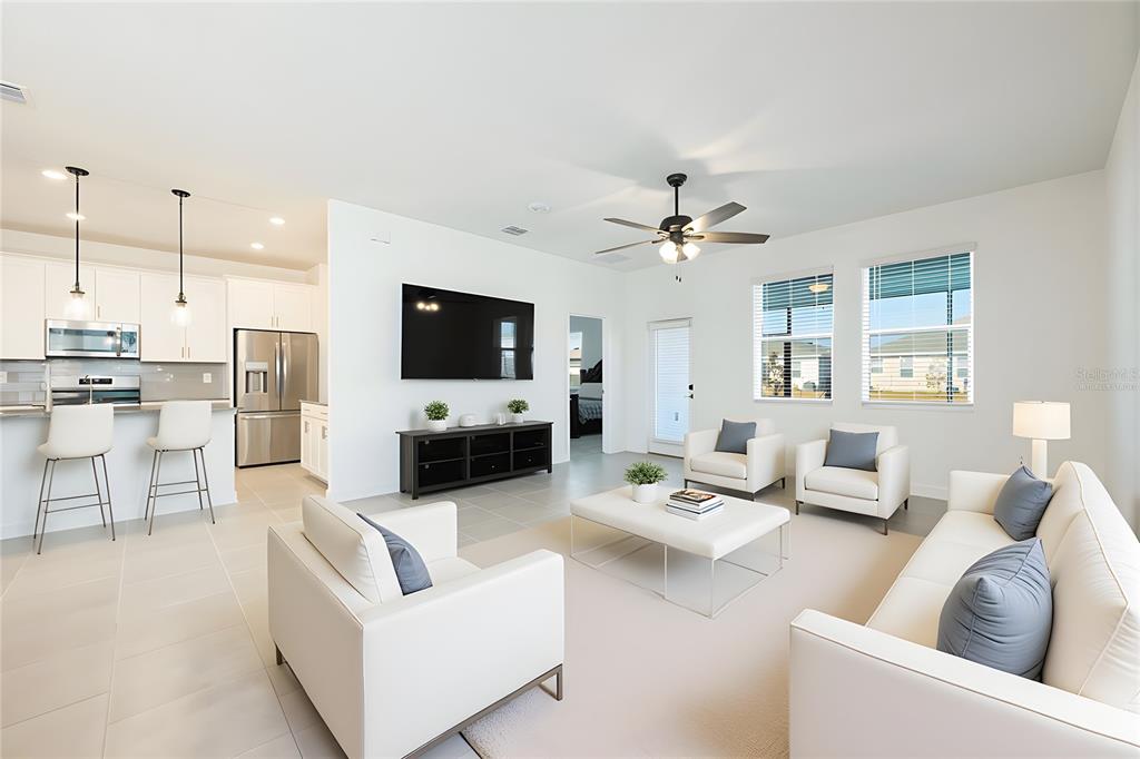 A bright open-concept living room features white furniture, a television, and an adjacent kitchen — 1874 FLOURISH AVENUE, KISSIMMEE, FL