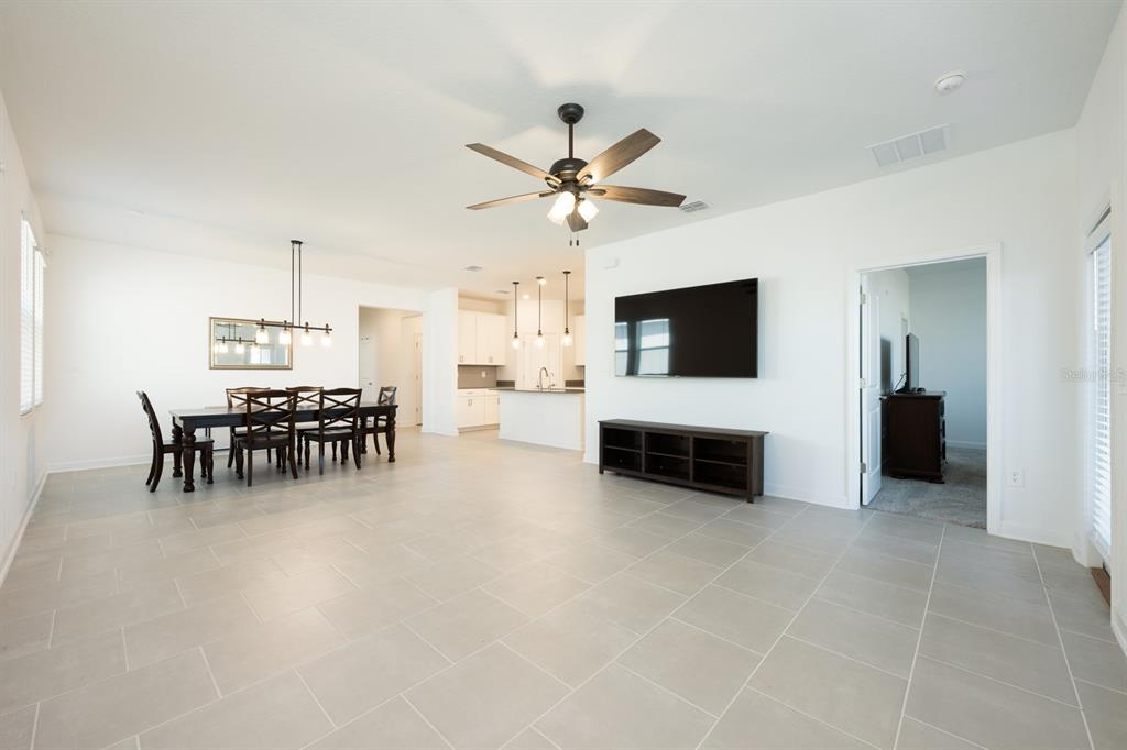 An open-concept living and dining area features white walls, tile flooring, and a ceiling fan — 1874 FLOURISH AVENUE, KISSIMMEE, FL